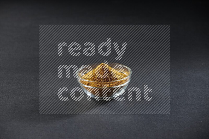 A glass bowl full of turmeric powder on black flooring