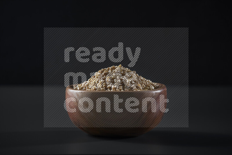 Hulled wheat in a wooden bowl on grey background