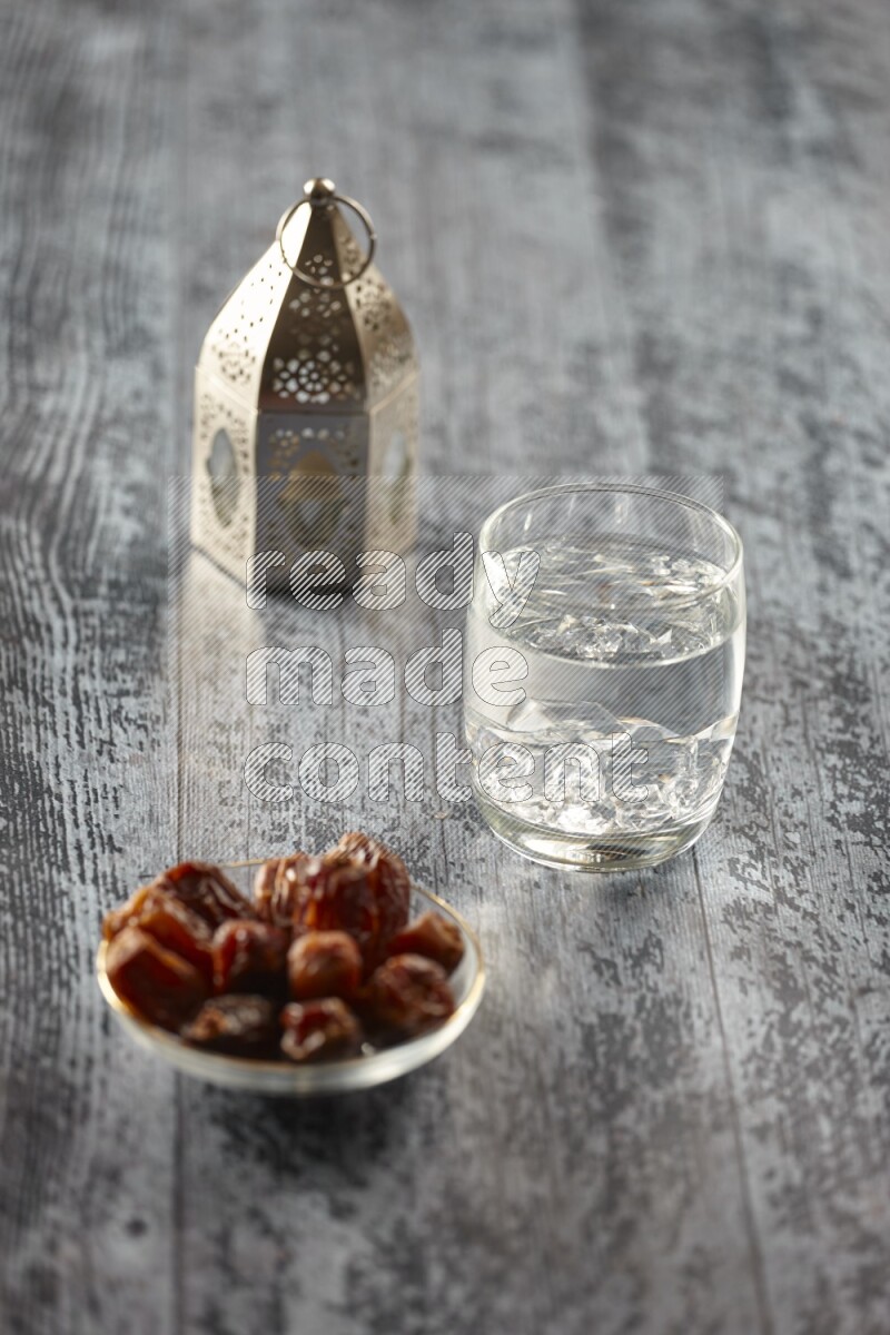 A silver lantern with different drinks, dates, nuts, prayer beads and quran on grey wooden background