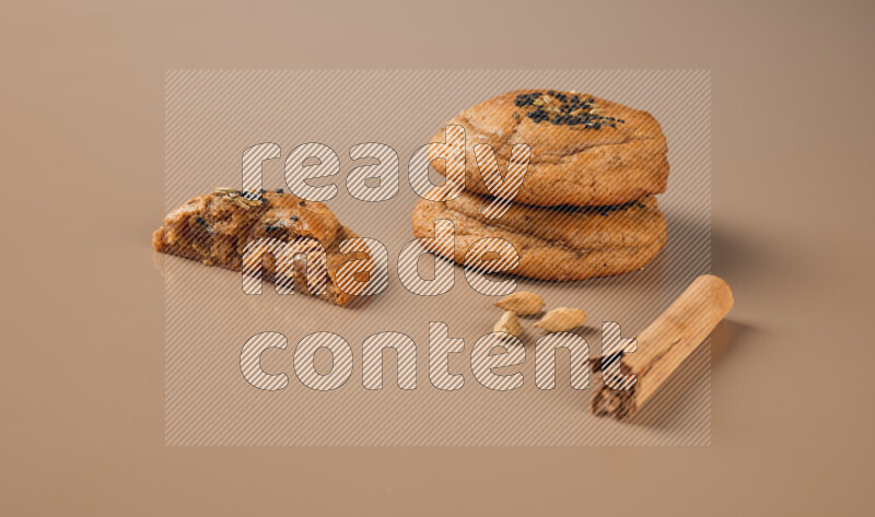 Three chocolate chip cookies beside cinimon sticks on a brown background
