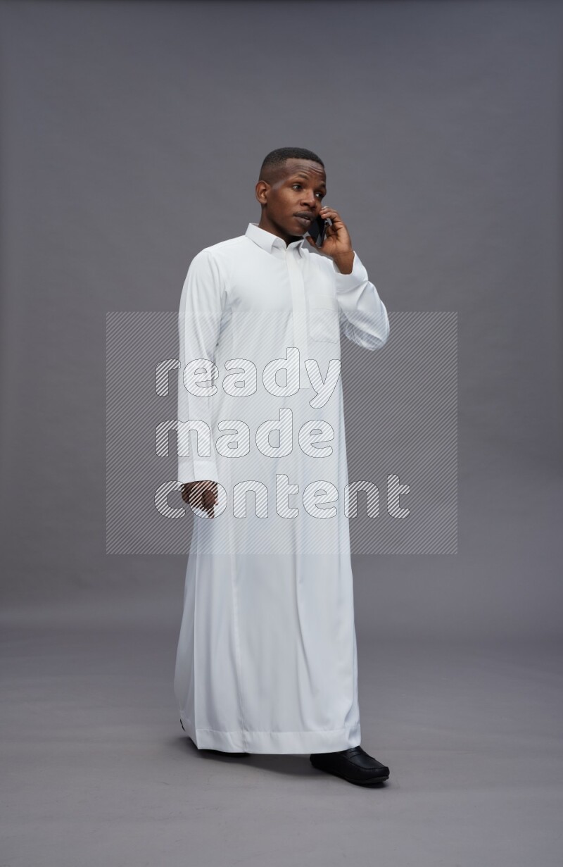 Saudi man wearing thob standing talking on phone on gray background