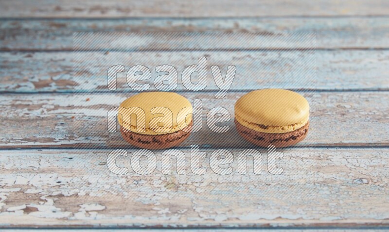 45º Shot of two Yellow and Brown Chai Latte macarons on light blue wooden background