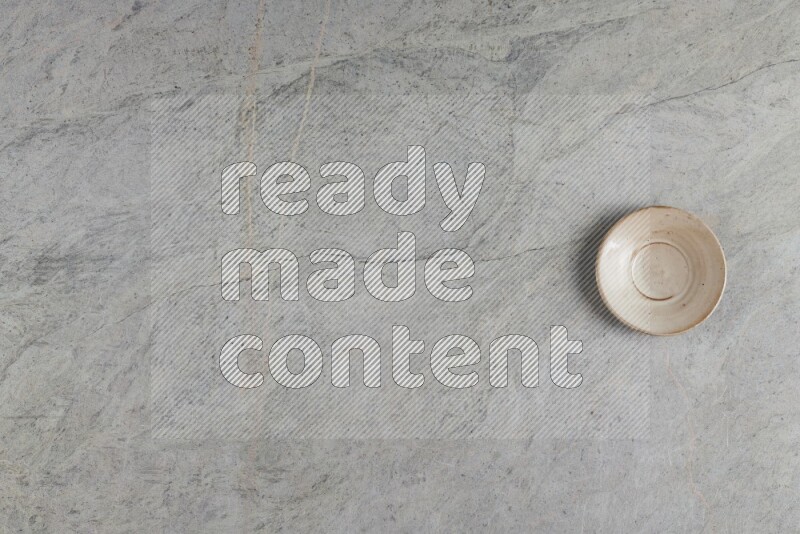 A circular beige pottery plate on grey marble background