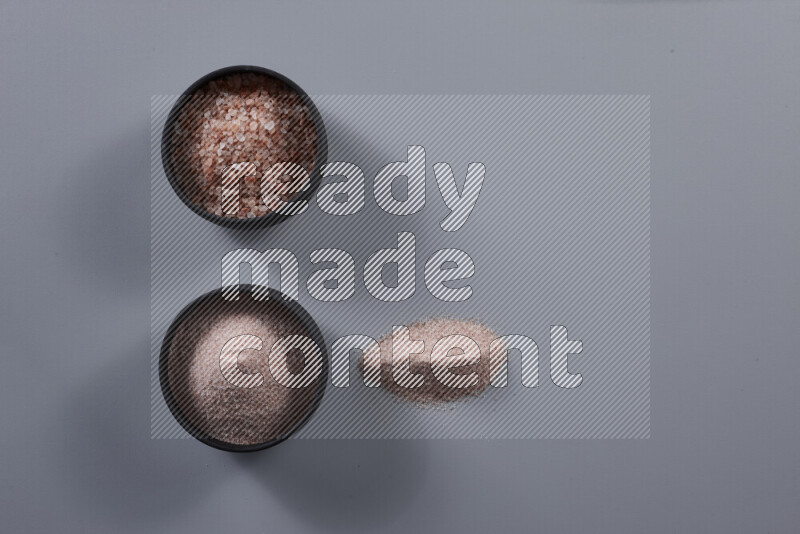 2 pottery bowls one is filled with fine himalayan salt and the other with coarse himalayan salt on grey background