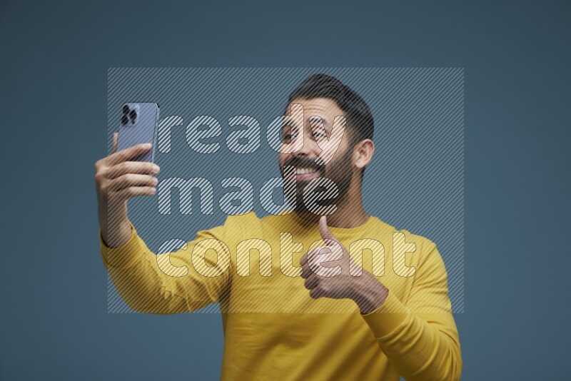 Man Taking a Selfie  in a blue background wearing a yellow shirt