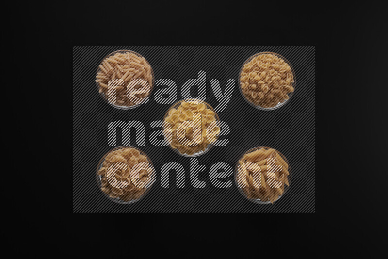 Different pasta types in 5 glass bowls on black background