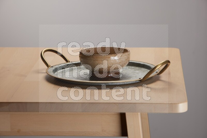 multicolored bowl placed on a rounded stainless steel tray with golden handels on the edge of wooden table