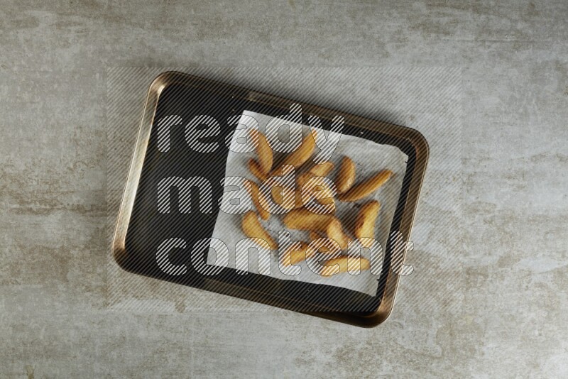 wedges potato on parchment paper in a black stainless steel rectangle tray on grey textured counter top