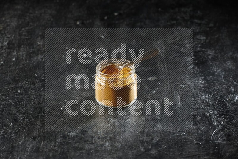 وعاء زجاجي وملعقة معدنية ممتلئان ببودرة الكركم على خلفية سوداء