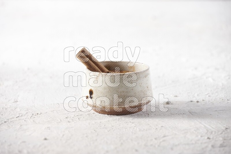 Ceramic beige bowl full of cinnamon powder with a cinnamon stick on a textured white background