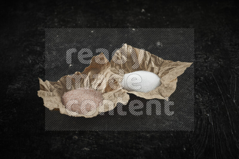 2 crumpled pieces of paper full of pink himalayan salt and white salt on black background
