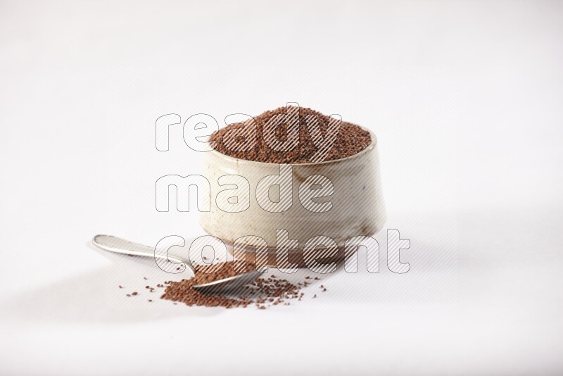 A beige pottery bowl and a metal spoon full of garden cress seeds on a white flooring