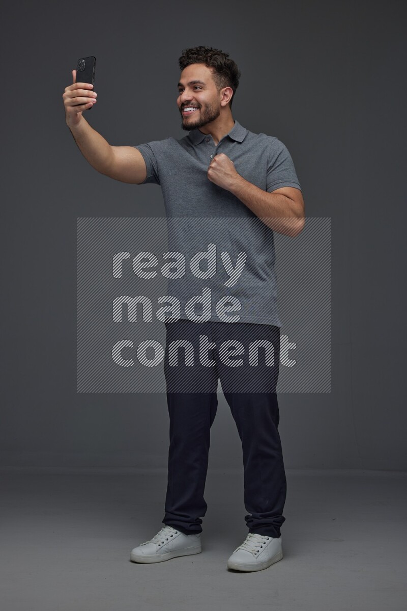 A man wearing casual and taking selfie with his phone different angles eye level on a gray background