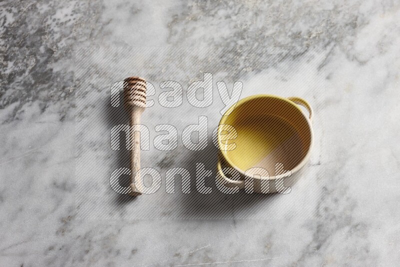 Multicolored pottery bowl with wooden honey dipper on the side on grey marble background