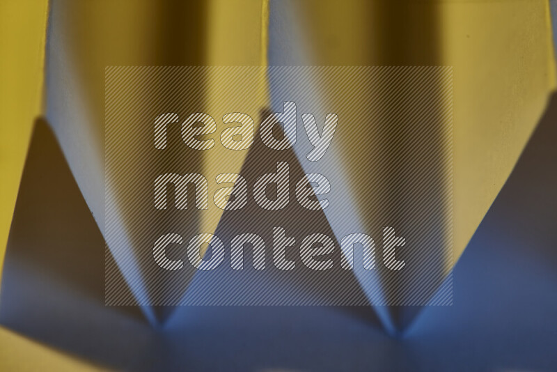 A close-up abstract image showing sharp geometric paper folds in blue gradients and warm tones