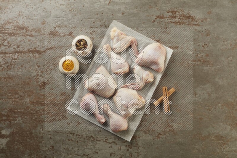 Mixed fresh chicken pieces on a parchment paper direct on a textured rustic background