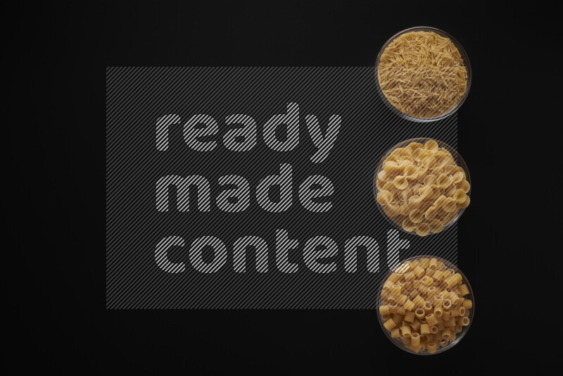 Different pasta types in 3 glass bowls on black background