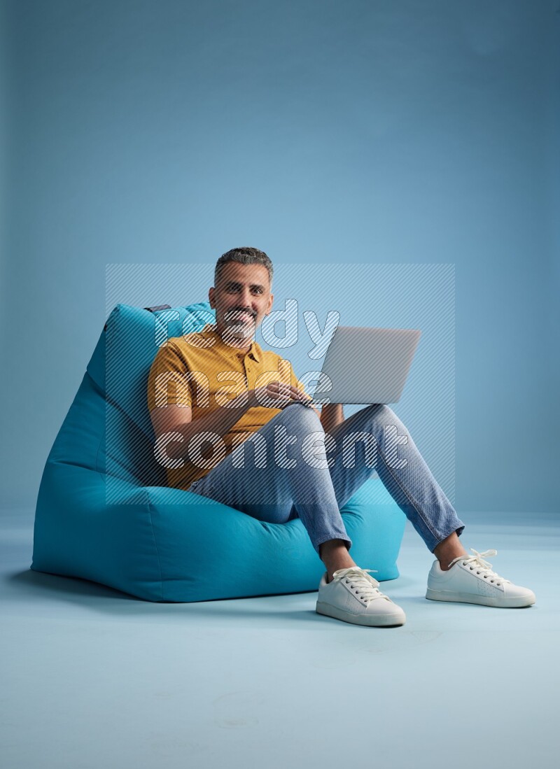 A man sitting on a blue beanbag and working on laptop