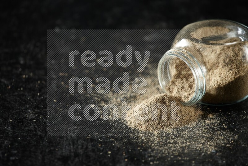 وعاء زجاجي للتوابل مقلوب ممتلئ ببودرة الهيل على خلفية سوداء