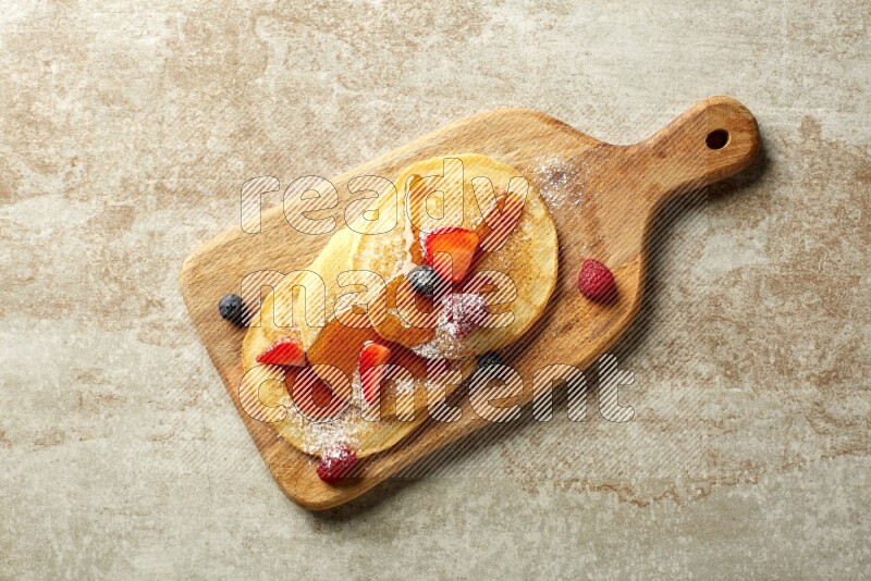 Three stacked mixed berries pancakes on a wooden board on beige background
