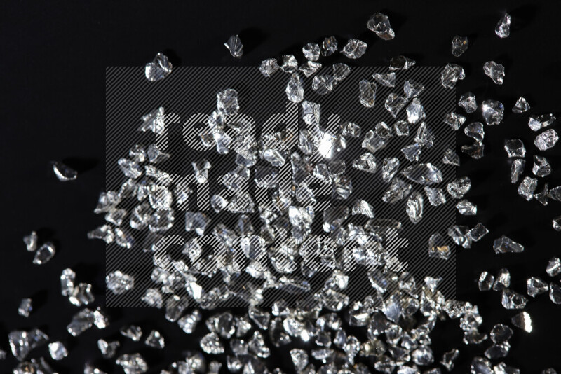 Silver shimmering fragments of glass scattered on a black background