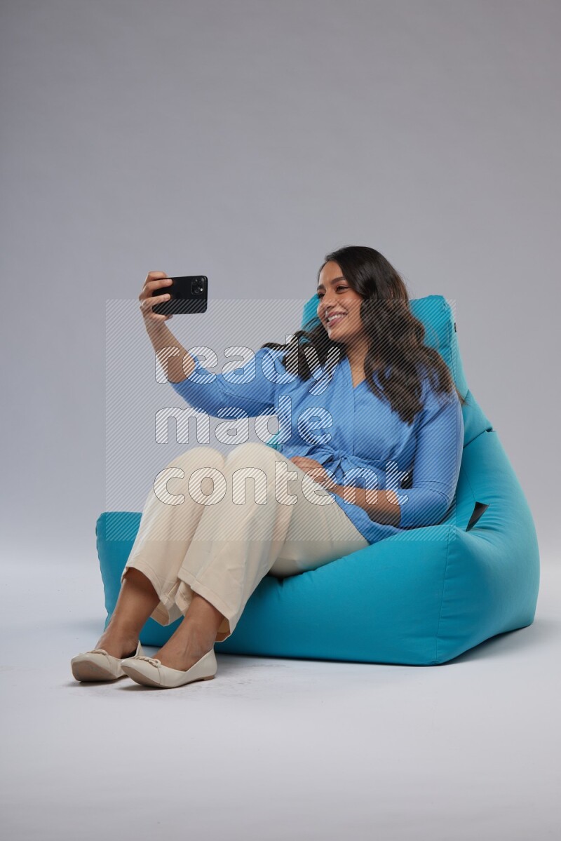 A woman sitting on a blue beanbag and taking selfie
