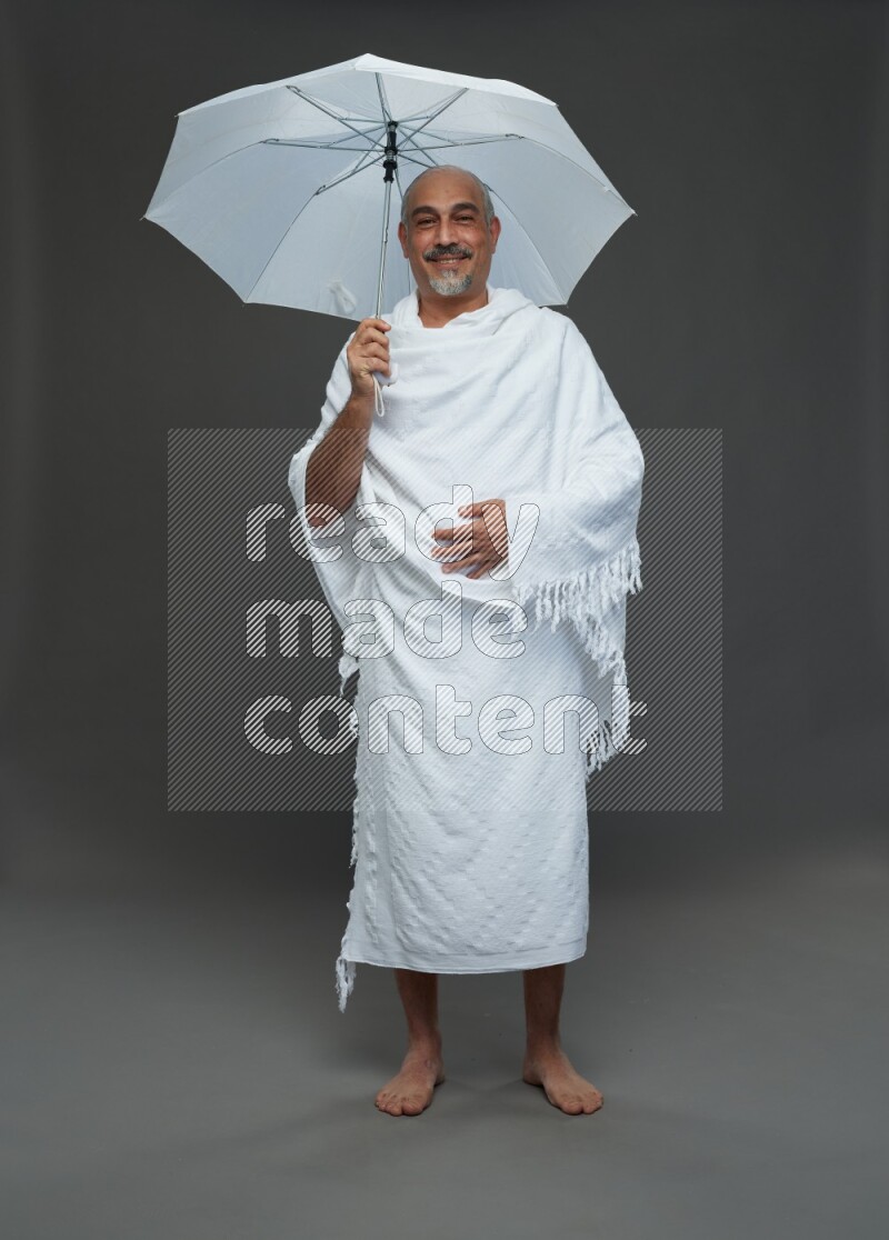A man wearing Ehram Standing holding umbrella on gray background