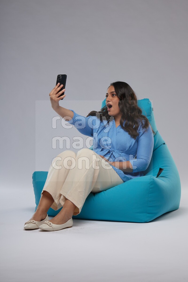 A woman sitting on a blue beanbag and taking selfie