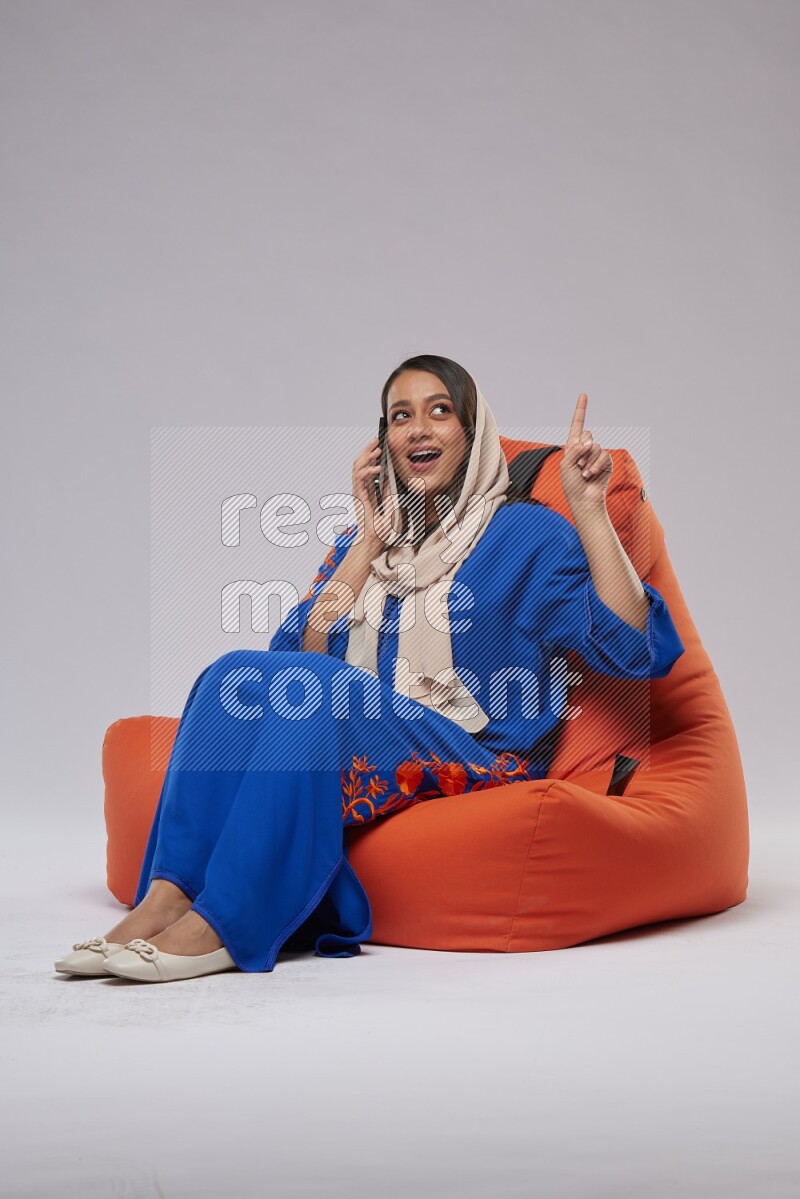 A Saudi woman wearing Jalabiya sitting on an orange beanbag and talking on the phone