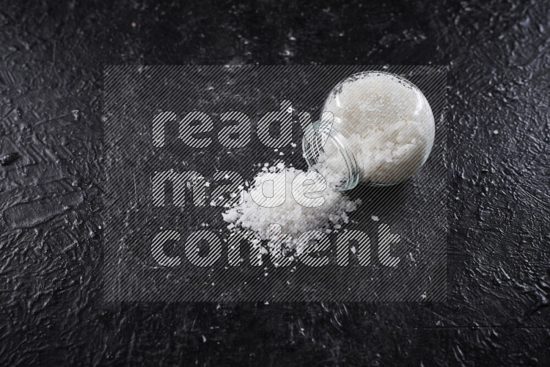 A glass jar full of coarse sea salt crystals on black background