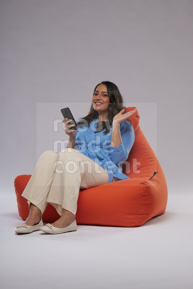 A woman sitting on an orange beanbag and texting on phone