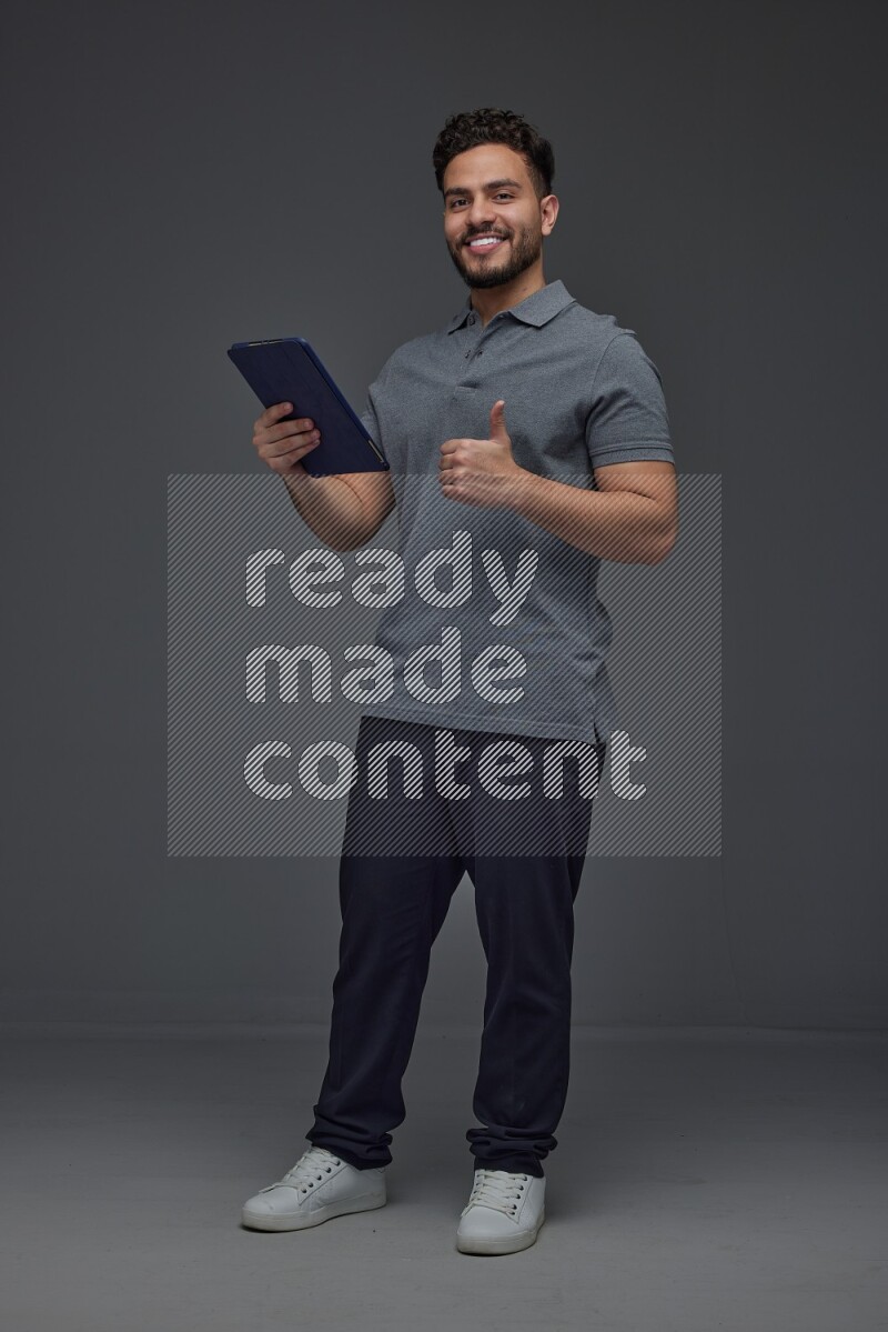 A man wearing casual standing and using his tablet and making multi hand gestures different angles eye level on a gray background