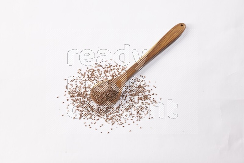 A wooden ladle full of flax seeds on a white flooring