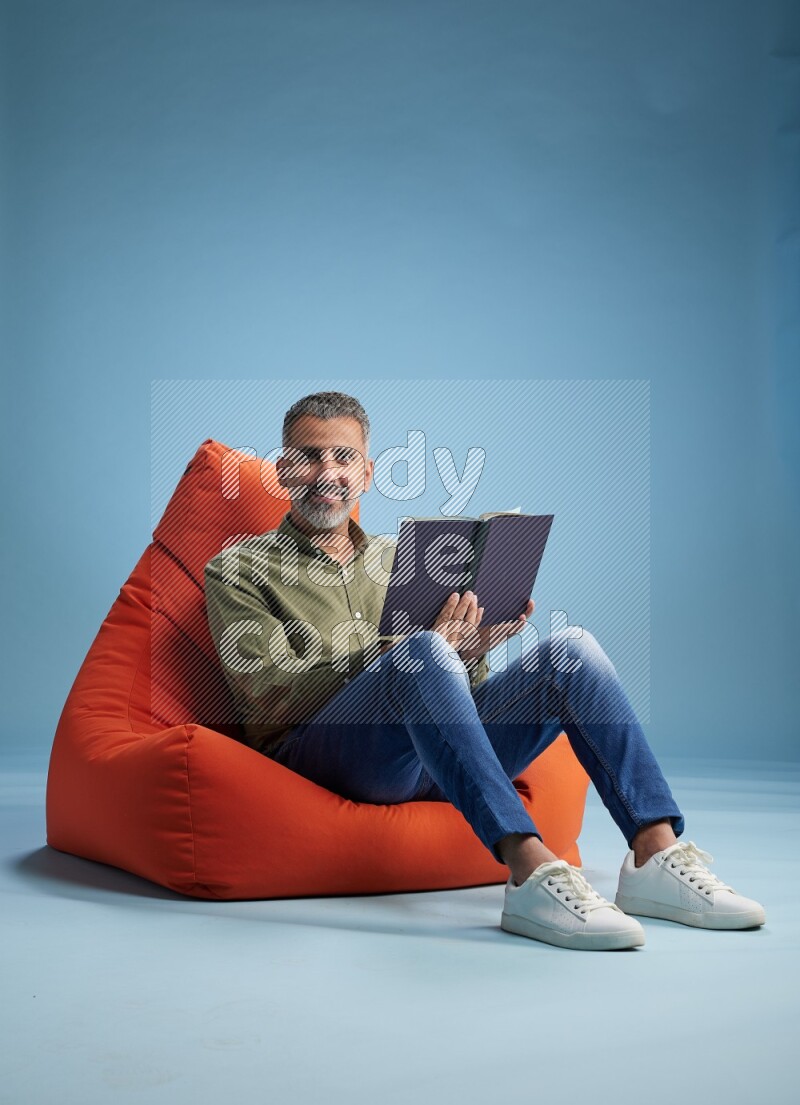 A man sitting on an orange beanbag and reading a book