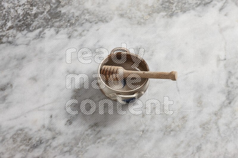 Multicolored pottery bowl with wooden honey dipper in it on grey marble background