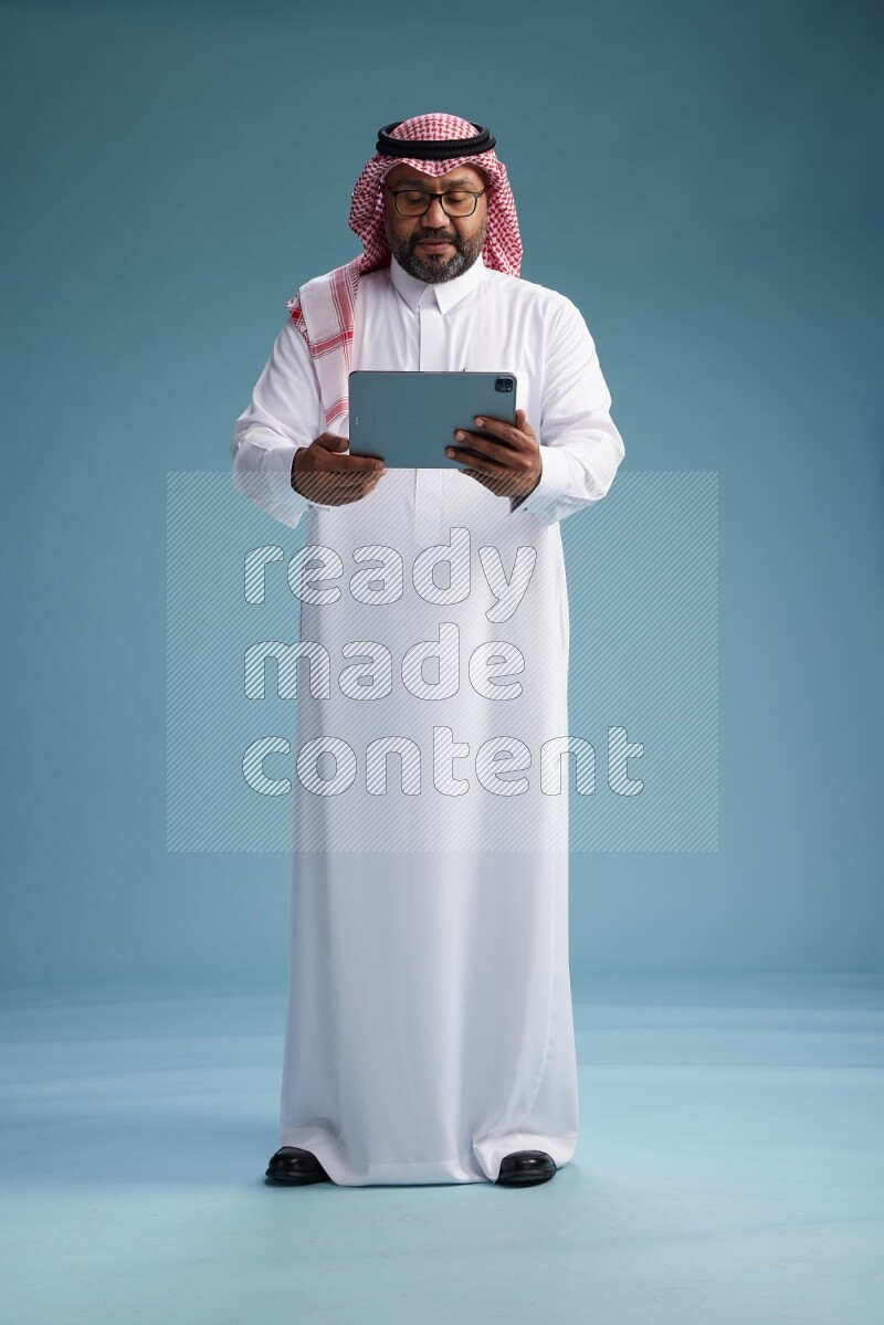 Saudi Man with shimag Standing holding a tablet on blue background