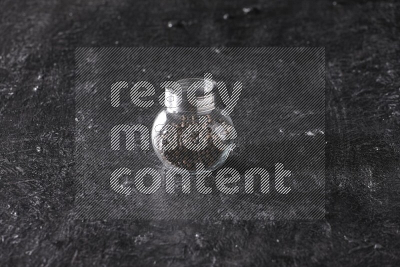 حبوب الفلفل الأسود في وعاء زجاجي علي خلفية سوداء