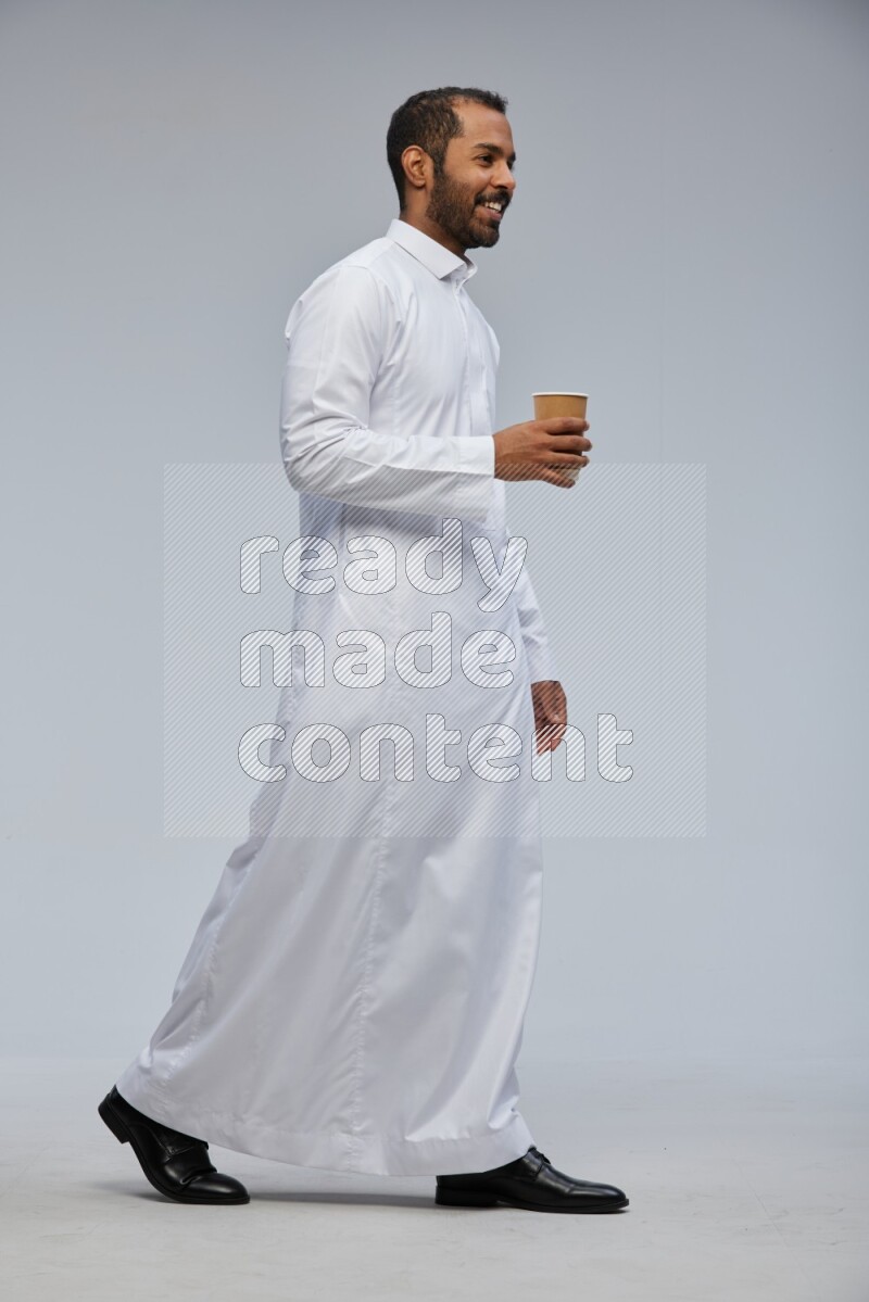 Saudi man wearing thob standing holding paper cup on gray background