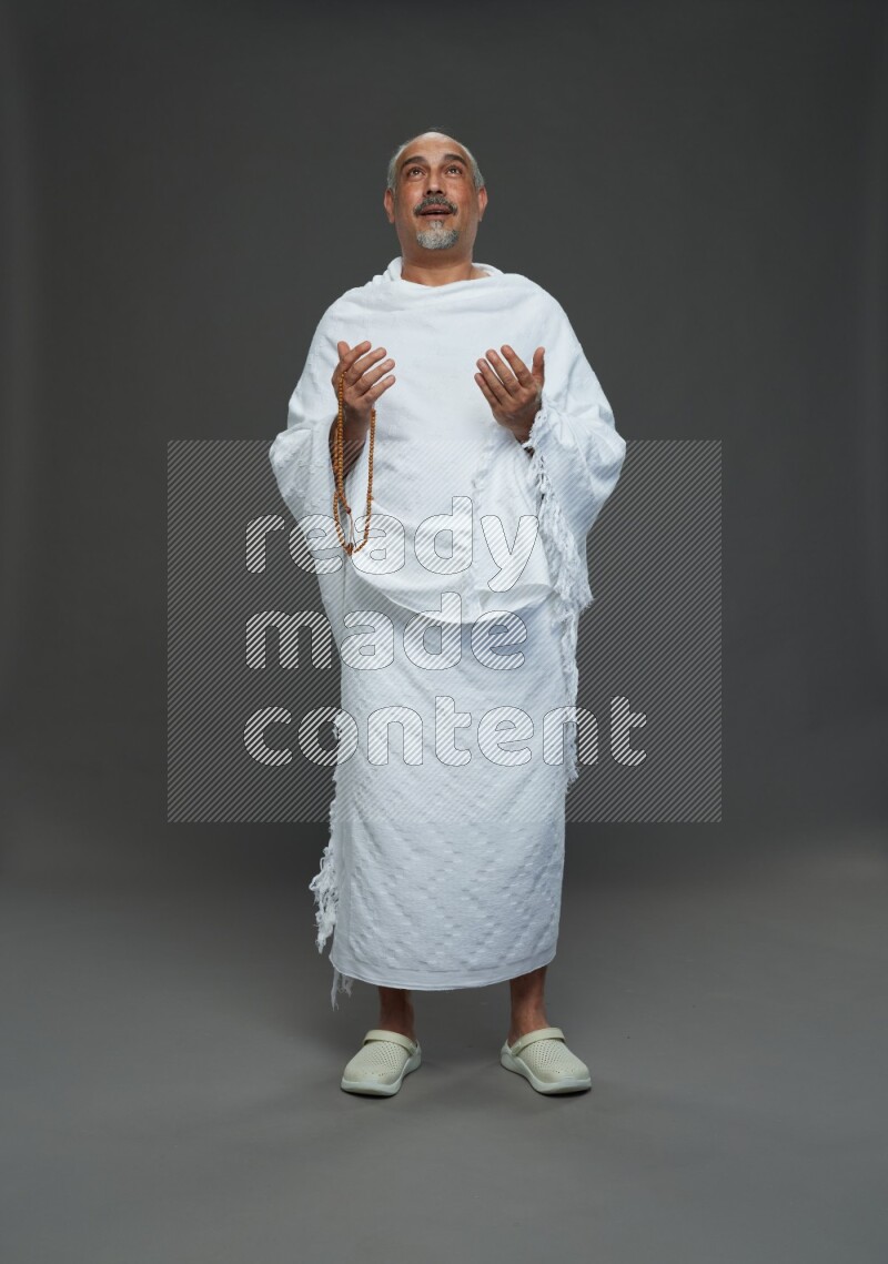 A man wearing Ehram Standing dua'a on gray background
