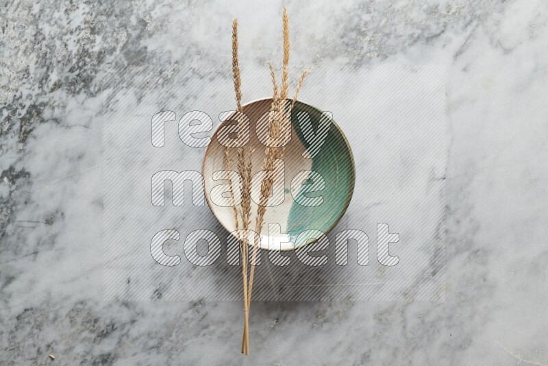 Wheat stalks on multicolored pottery plate on grey marble background
