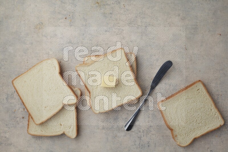 White toast slices with a butter cube and a spreading knife on a light blue textured background