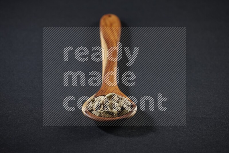 A wooden ladle full of cardamom on black flooring