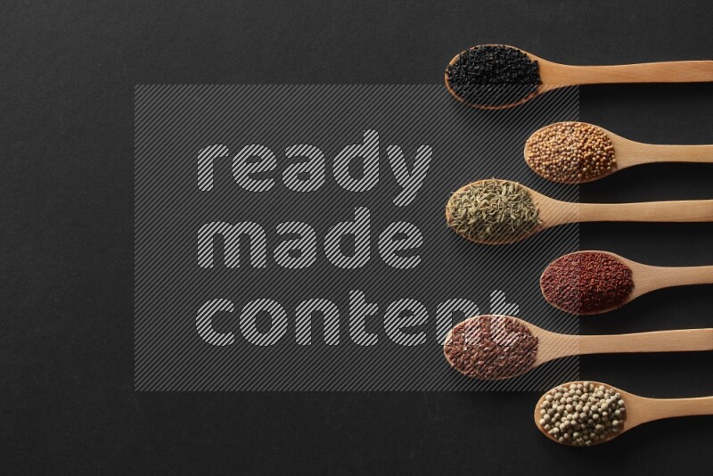 الفلفل الأسود وحبوب الخردل وحبة البركة وحب الرشاد والكمون و حبوب الكتان في معالق خشبية علي خلفية سوداء