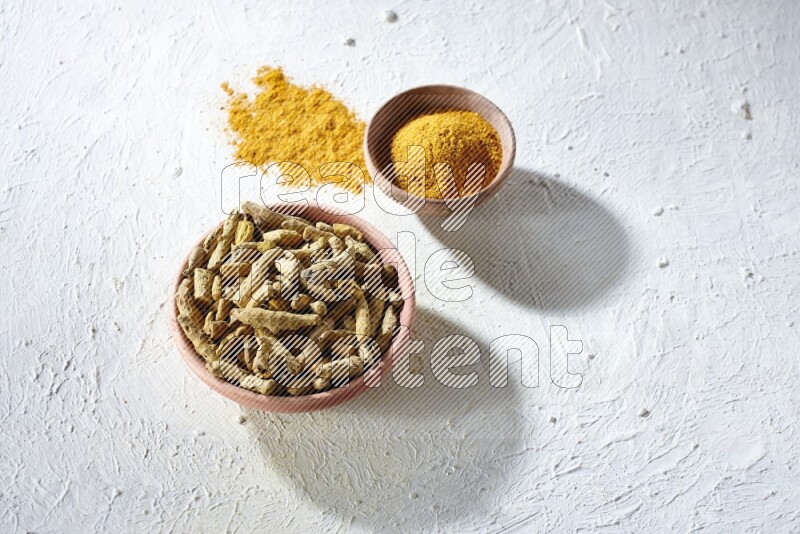 وعاءان خشبيان، أحدهما ممتلئ ببودرة الكركم والآخر بأصابع الكركم المجففة، على خلفية بيضاء