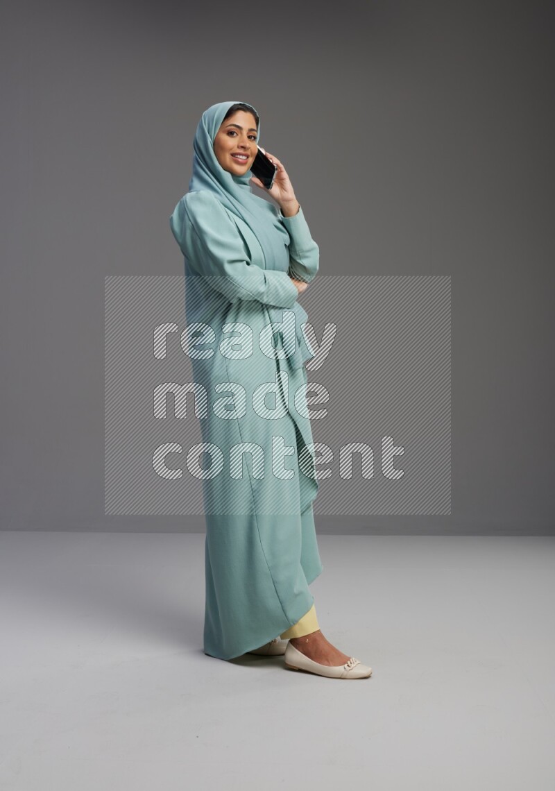 Saudi Woman wearing Abaya standing talking on phone on Gray background