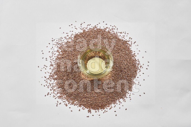 A glass jar full of flaxseeds oil surrounded by flax seeds on a white flooring