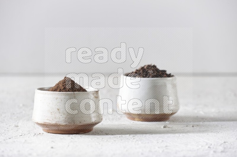 2 Beige ceramic bowls, one full of cloves and the other full of powder on textured white flooring