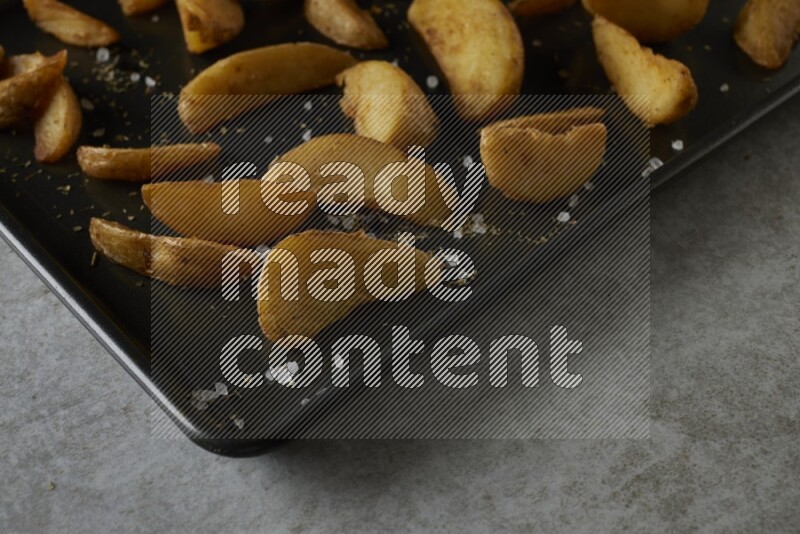 wedges potato in a black stainless steel rectangle tray on grey textured counter top