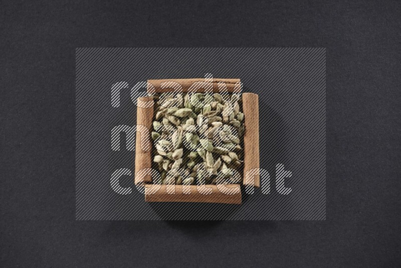 أربعة من أعواد القرفة مكونة شكل مربع بداخلها حبوب الهيل علي خلفية سوداء