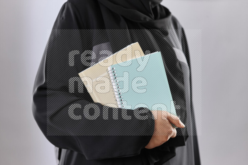 A woman in abaya holding books and a board in different positions (back to school)